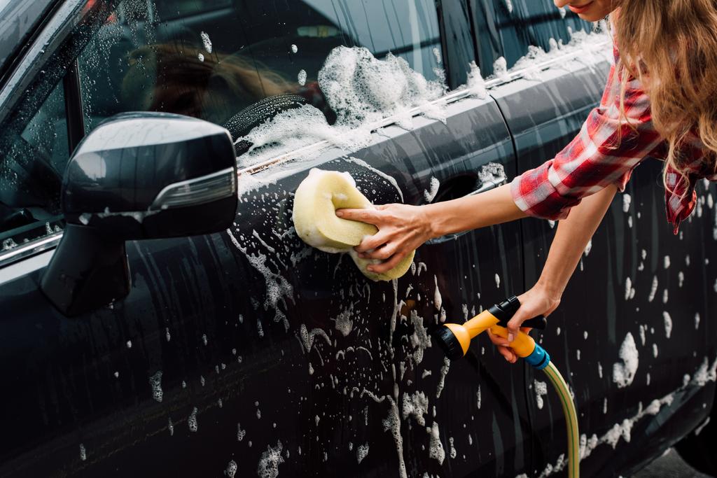 обрезанный вид молодой женщины, моющей мокрую машину в пене с губкой
 - Фото, изображение