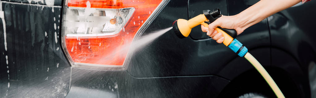 panoramatický záběr dívčí ženy mytí černého auta a přidržením tlakové podložky  - Fotografie, Obrázek