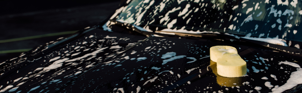 πανοραμικό κίτρινο σφουγγάρι σε βρεγμένο και πολυτελές μαύρο αυτοκίνητο στο πλύσιμο του αυτοκινήτου  - Φωτογραφία, εικόνα