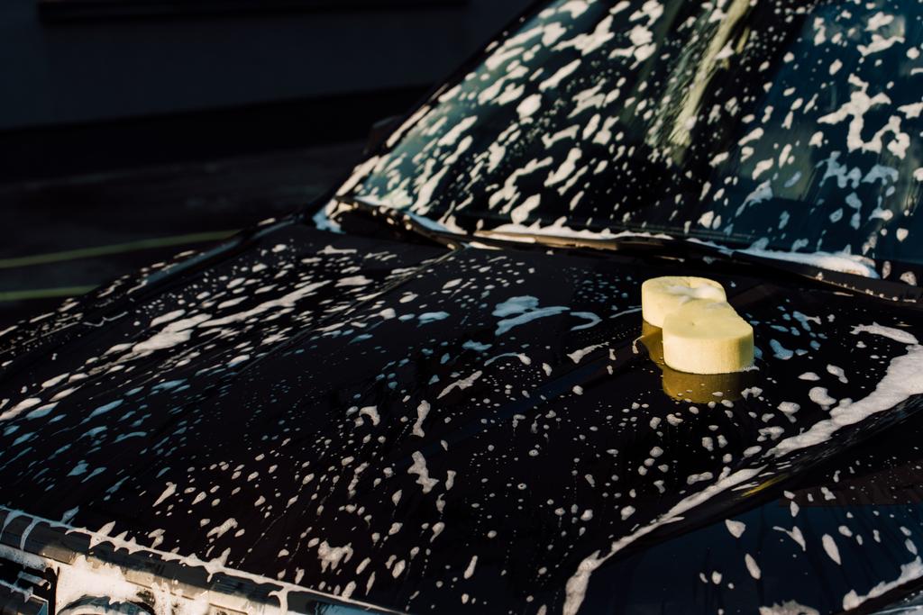 Gelber Schwamm auf nassem und luxuriösem schwarzen Auto in der Waschanlage  - Foto, Bild