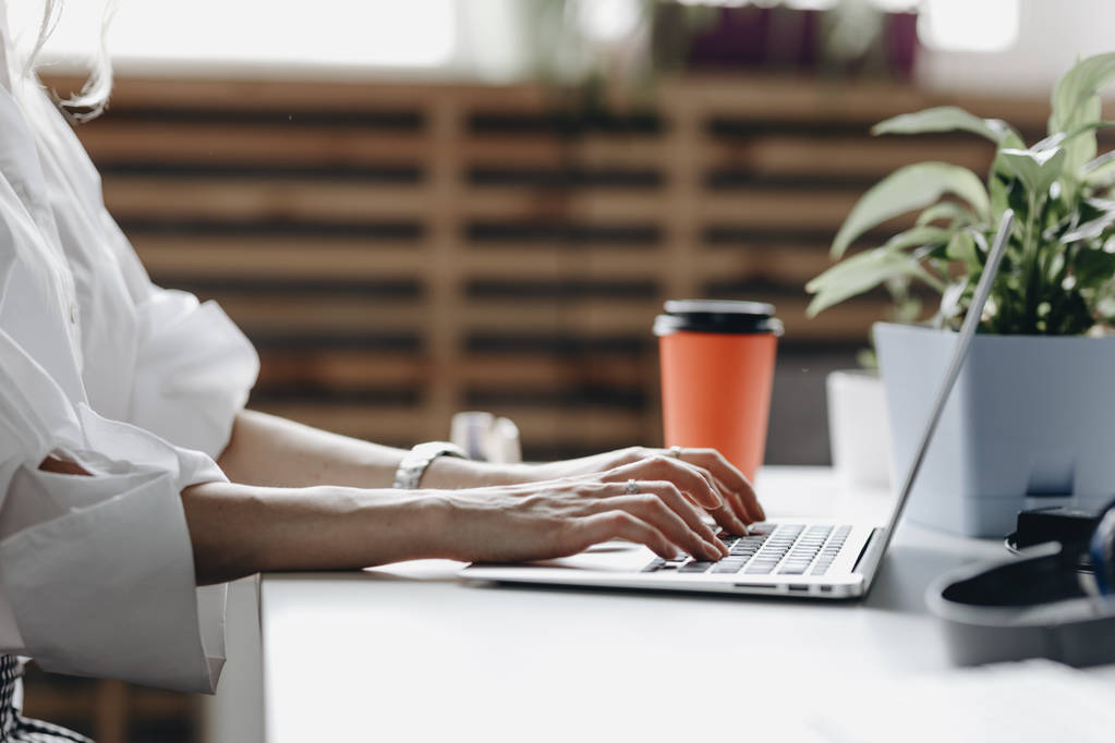 De vrouw gekleed in wit shirt werkt op de laptop zittend aan de balie in een lichte moderne open ruimte kantoor - Foto, afbeelding