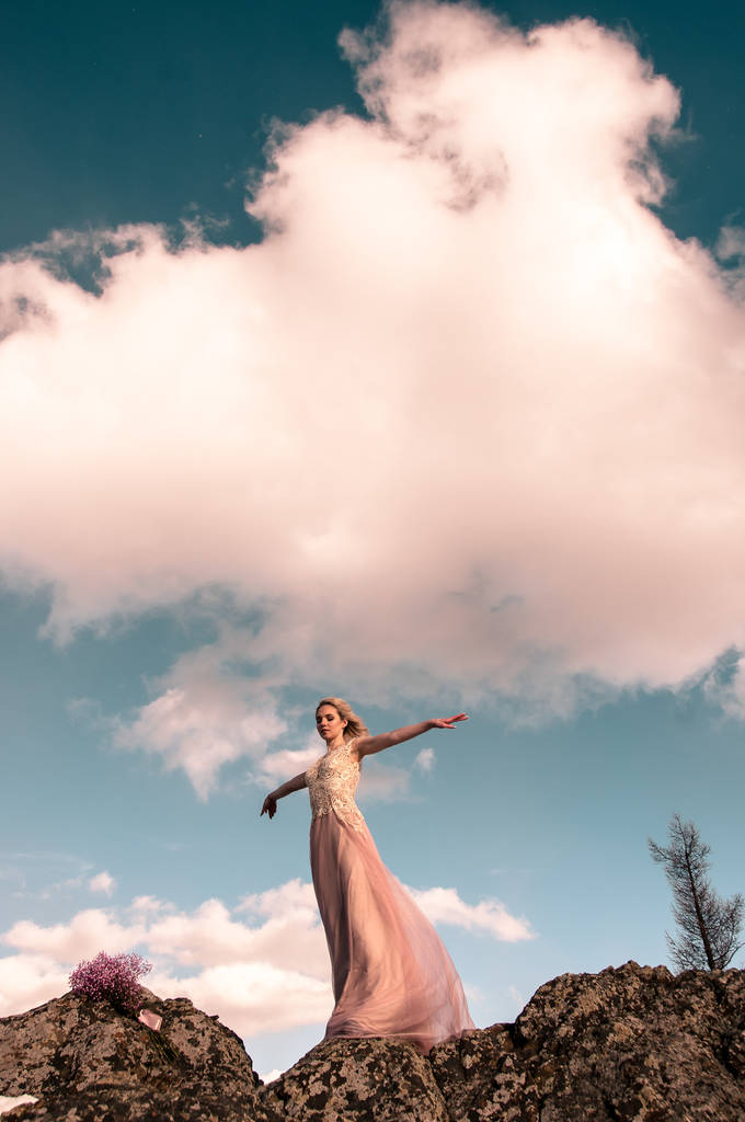 Tyttö iltapuvussa vuorilla pilvistä taivasta vasten
 - Valokuva, kuva