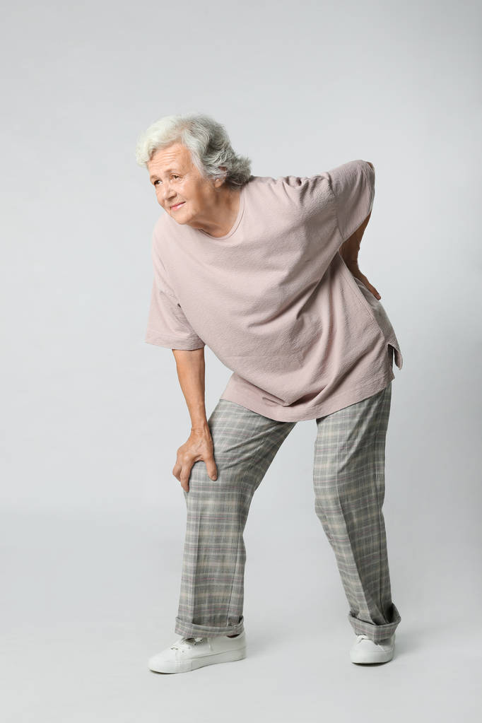 Ganzkörperporträt einer Seniorin mit Knieproblemen auf grauem Hintergrund - Foto, Bild
