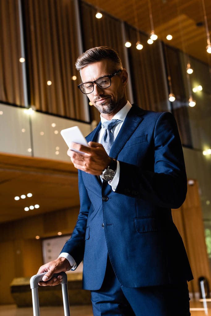 красивий бізнесмен в костюмі і окулярах, використовуючи смартфон в готелі
 - Фото, зображення