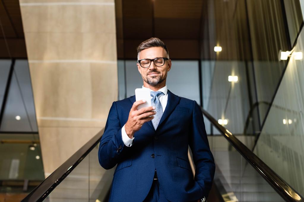 красивый бизнесмен в костюме и очках с помощью смартфона в отеле
  - Фото, изображение