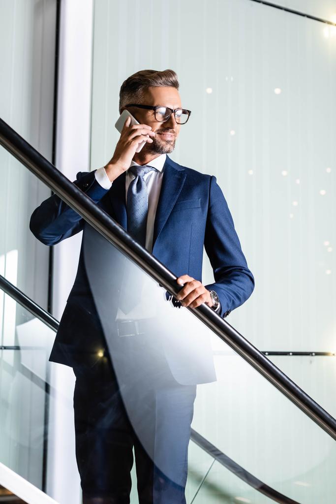 homem de negócios bonito em terno e óculos falando no smartphone
  - Foto, Imagem