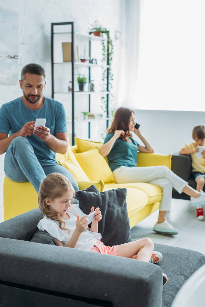 father with two children using smartphones while mother talking on smartphone at home - Photo, Image