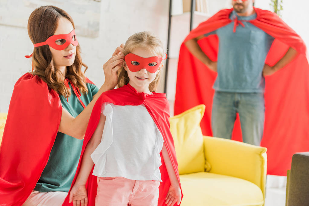Äiti puku supersankari pukeutuminen tytär, kun isä seisoo kädet lantiolla
 - Valokuva, kuva