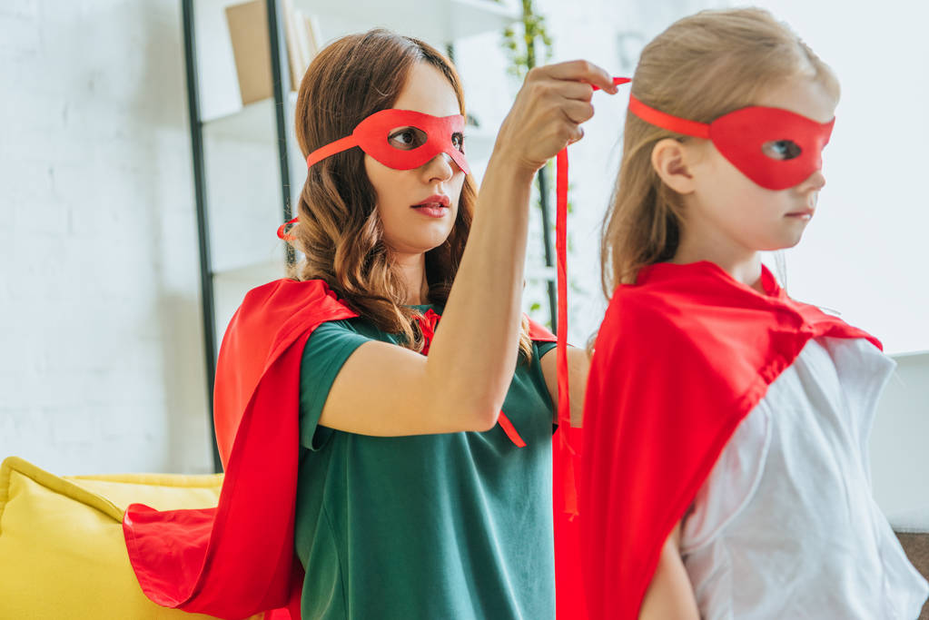 attente vrouw zetten masker van superheld op schattige dochter - Foto, afbeelding