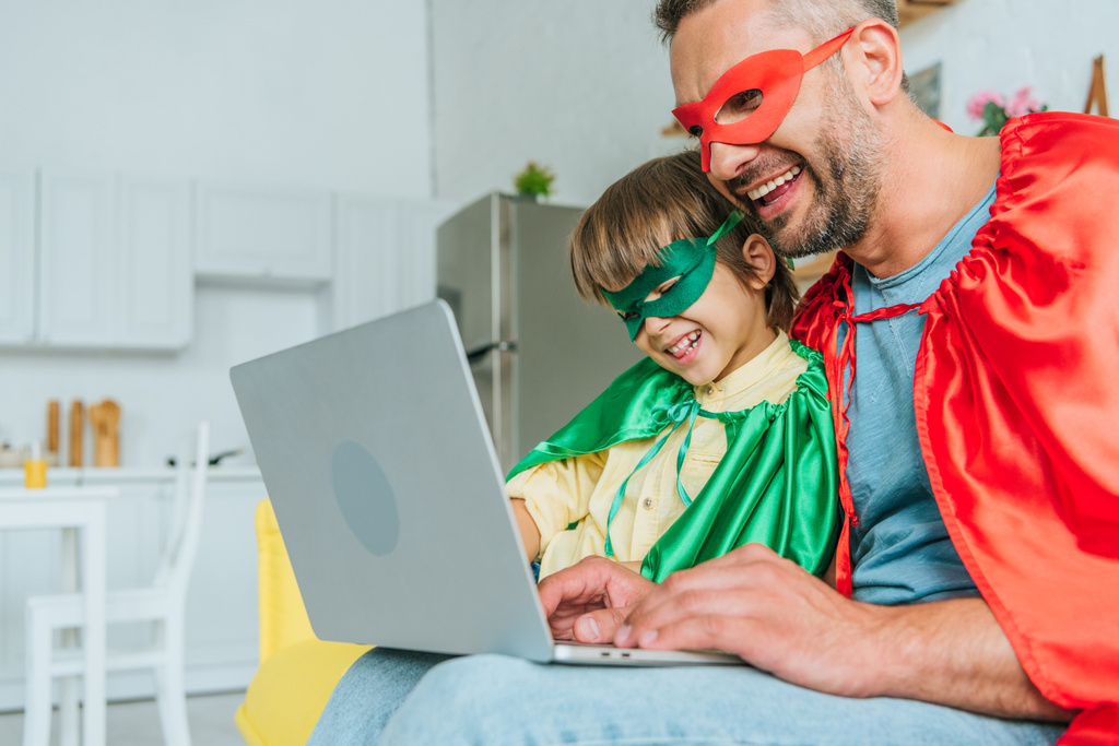 evde dizüstü bilgisayar kullanarak süper kahraman kostümleri neşeli baba ve oğlu - Fotoğraf, Görsel