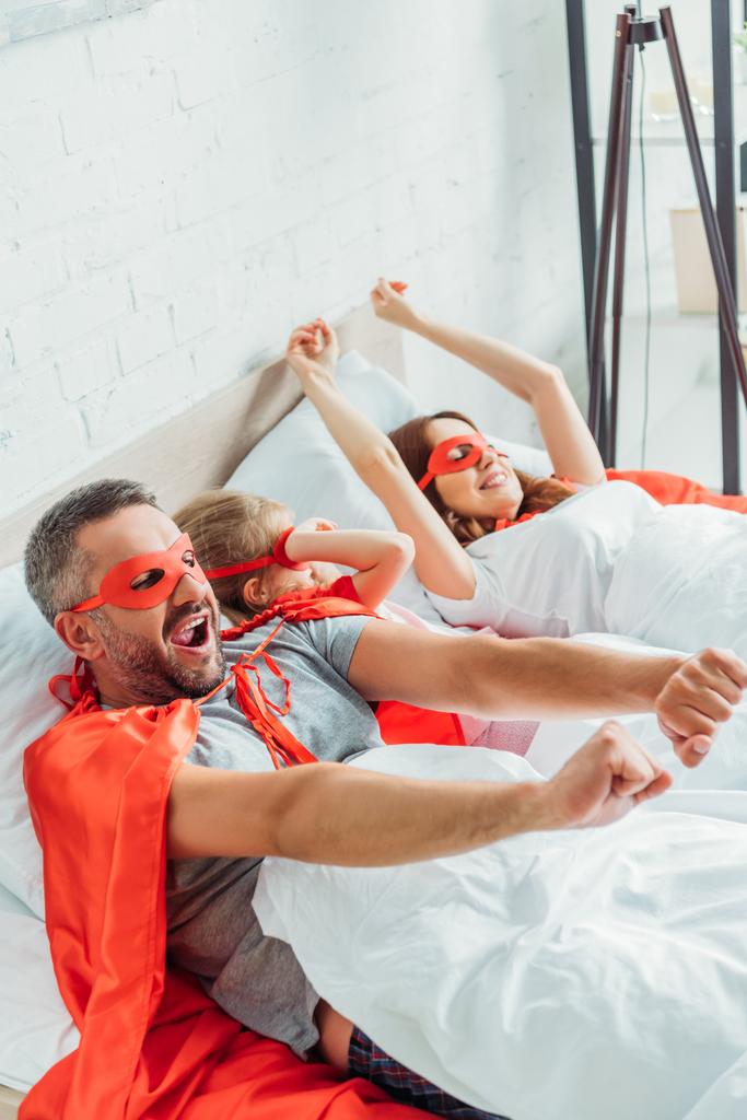 happy family in costumes of superheroes stretching while awakening in morning  - Photo, Image