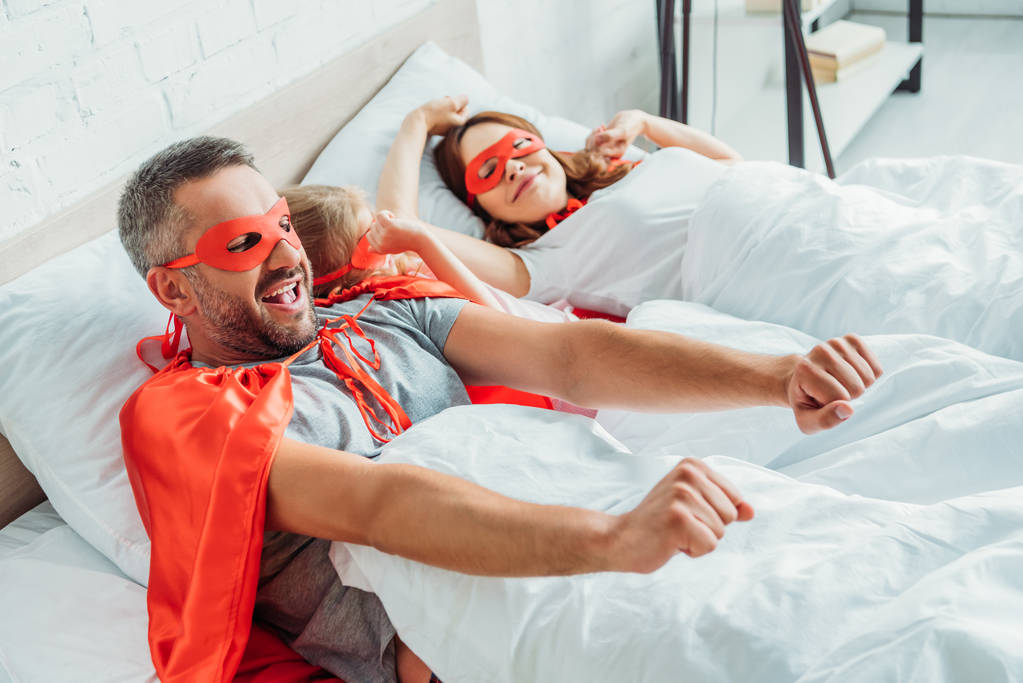 familia feliz en trajes de superhéroes estirándose mientras se despierta por la mañana
 - Foto, imagen