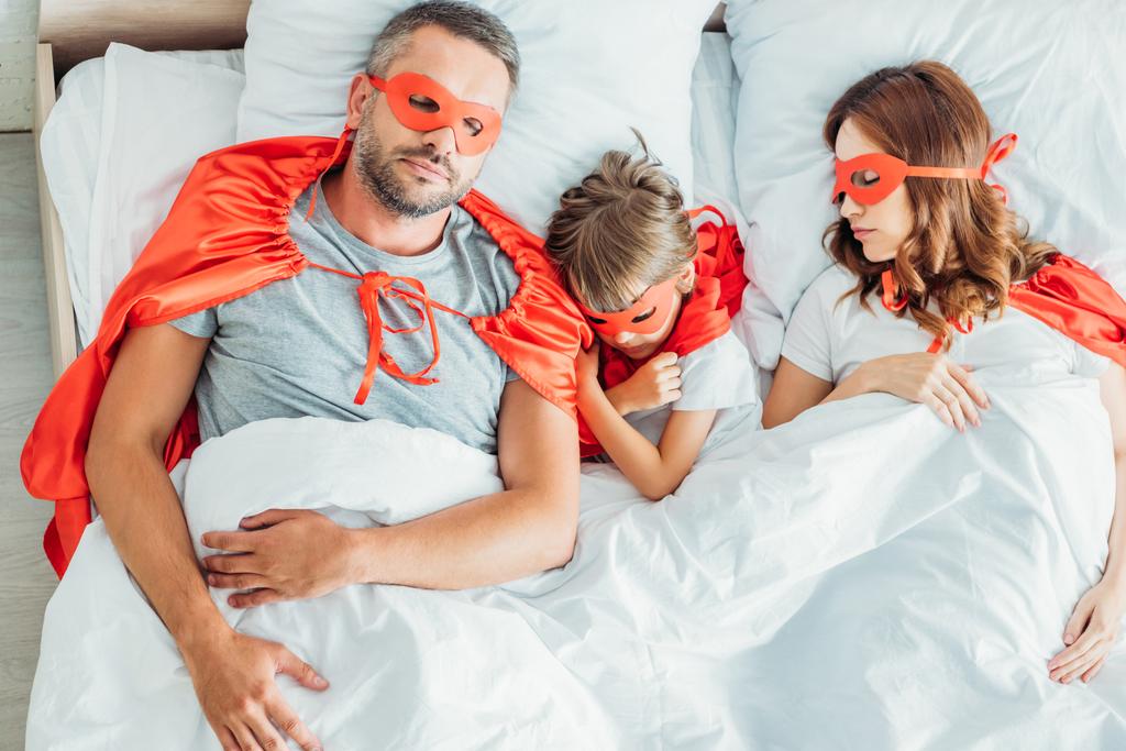 Top θέα πατέρας, μητέρα και γιος κοιμούνται στο κρεβάτι σε κοστούμια των υπερήρωες - Φωτογραφία, εικόνα