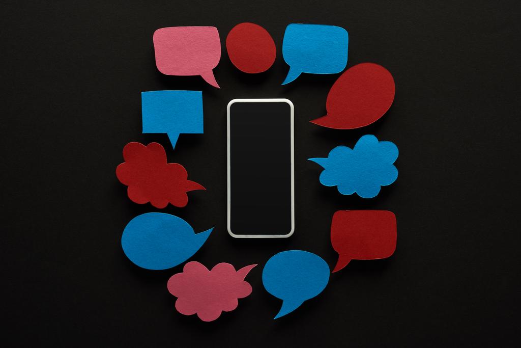 Ansicht von Smartphone mit leerem Bildschirm auf schwarzem Hintergrund mit leeren Sprechblasen, Cybermobbing-Konzept - Foto, Bild