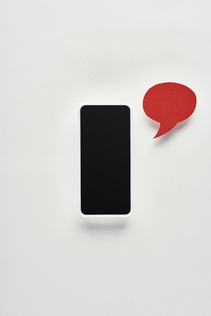 vista superior del teléfono inteligente con pantalla en blanco sobre fondo blanco cerca de burbuja de habla vacía roja, concepto de acoso cibernético
 - Foto, Imagen