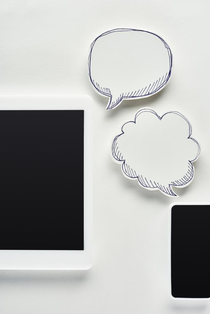 ylhäältä näkymä digitaalinen tabletti ja älypuhelin valkoisella taustalla lähellä tyhjää puhetta kuplia, verkkokiusaaminen käsite
 - Valokuva, kuva