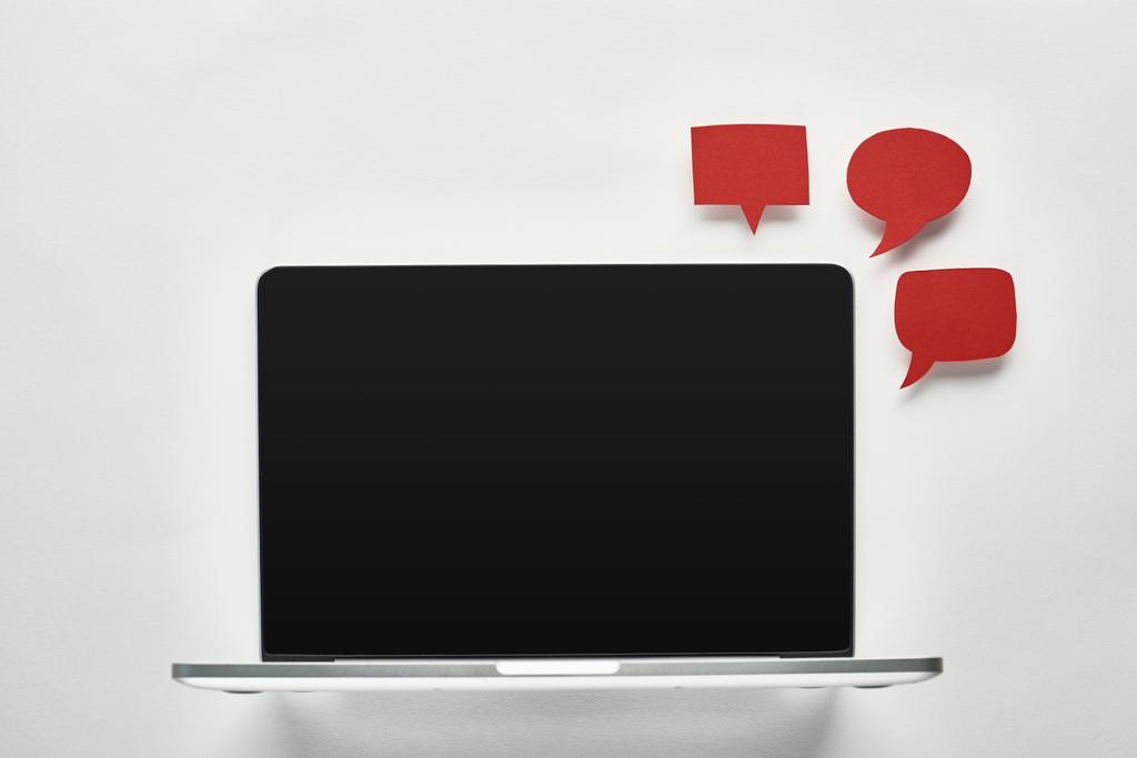 φορητό υπολογιστή με κενή οθόνη σε λευκό φόντο κοντά σε κενές κόκκινες φυσαλίδες ομιλίας, αντίληψη του κυβερνοεκφοβισμού - Φωτογραφία, εικόνα