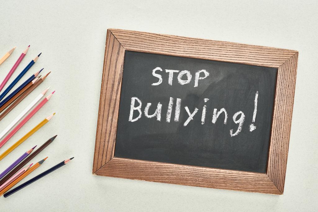vista superior de pizarra en marco de madera con letras stop bullying cerca de lápices de colores sobre fondo gris
 - Foto, Imagen