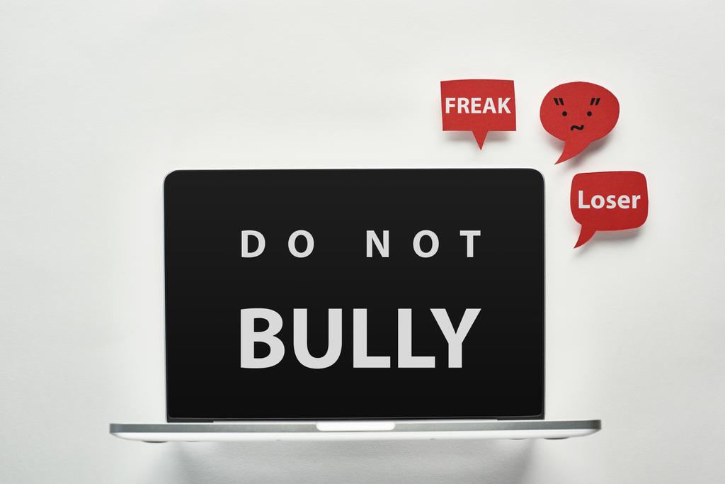 laptop with do not bully lettering on screen on white background near red speech bubbles with offensive words, cyberbullying concept - Photo, Image