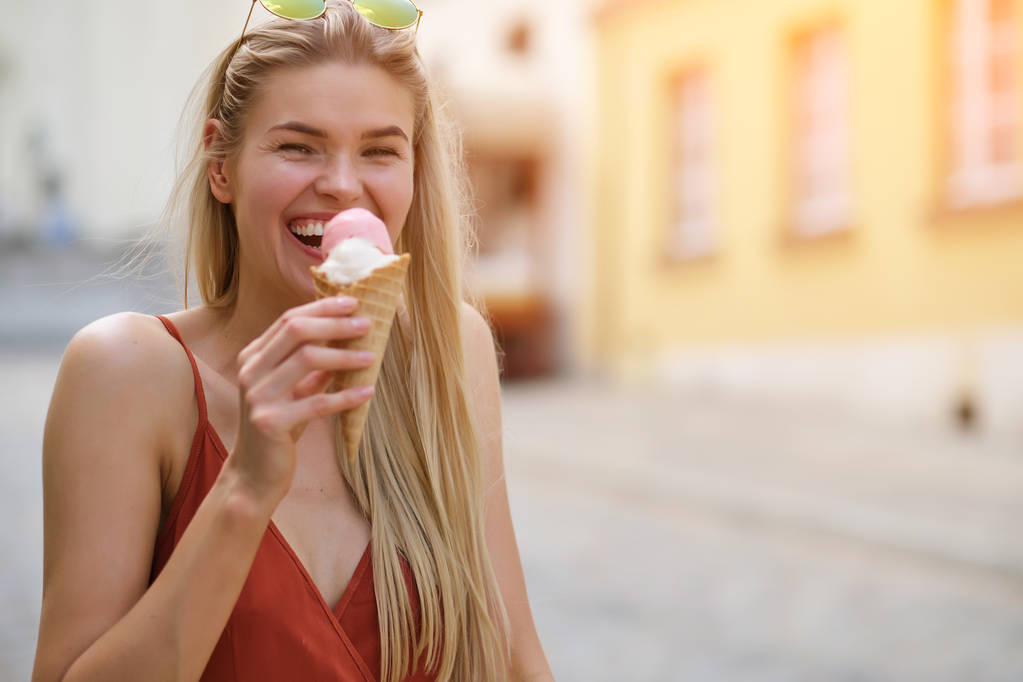 ένα ηλιόλουστο κορίτσι σε ένα καλοκαιρινό φόρεμα τρώει παγωτό και περπατά γύρω από t - Φωτογραφία, εικόνα