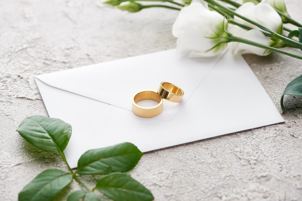 golden rings on white envelope near eustoma flowers on grey textured - Photo, Image