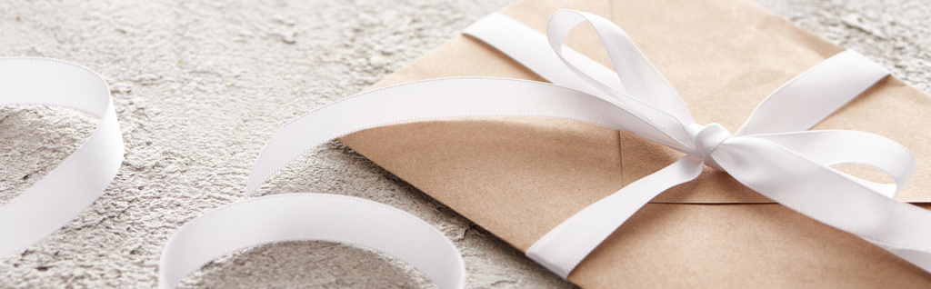panoramic shot of beige envelope with white ribbon on textured surface  - Photo, Image