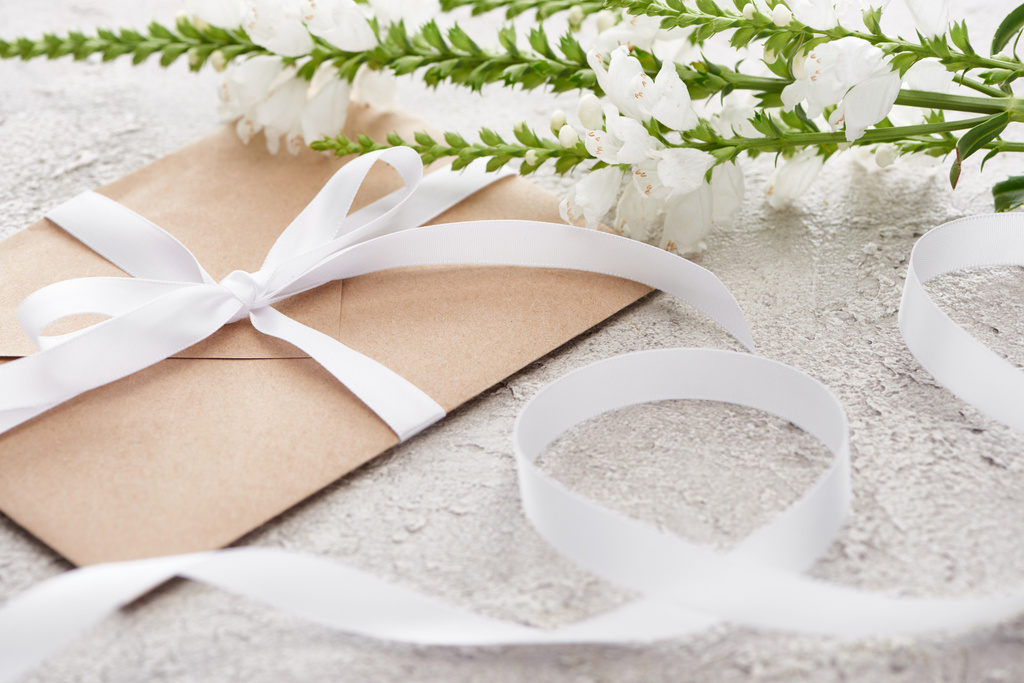 selective focus of beige envelope with ribbon near white flowers on textured surface   - Photo, Image