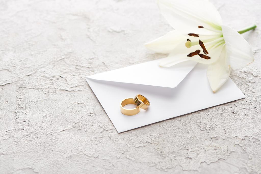 dokulu yüzeyde beyaz zambak yakınında zarf üzerinde iki altın alyans  - Fotoğraf, Görsel