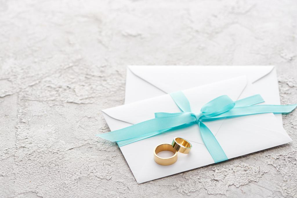két arany gyűrű fehér borítékon, kék szalaggal a textúrázott felületen - Fotó, kép