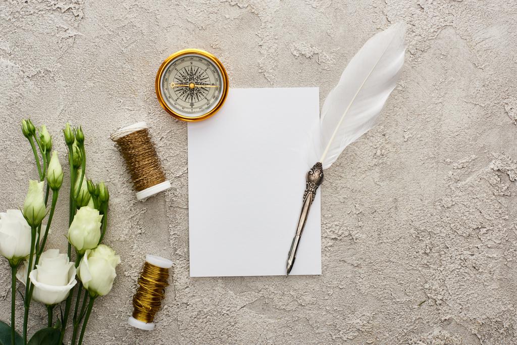 vista dall'alto della penna d'oca sulla carta bianca vicino alla bussola d'oro, bobine e fiori di eustoma bianco sulla superficie grigia testurizzata
 - Foto, immagini