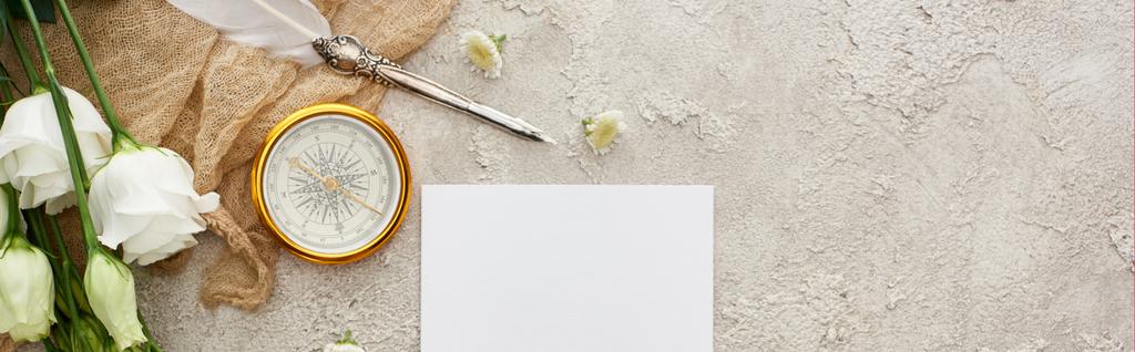 plano panorámico de pluma de pluma sobre tela de saco beige cerca de la tarjeta blanca, brújula dorada y flores eustoma en la superficie texturizada gris
 - Foto, imagen