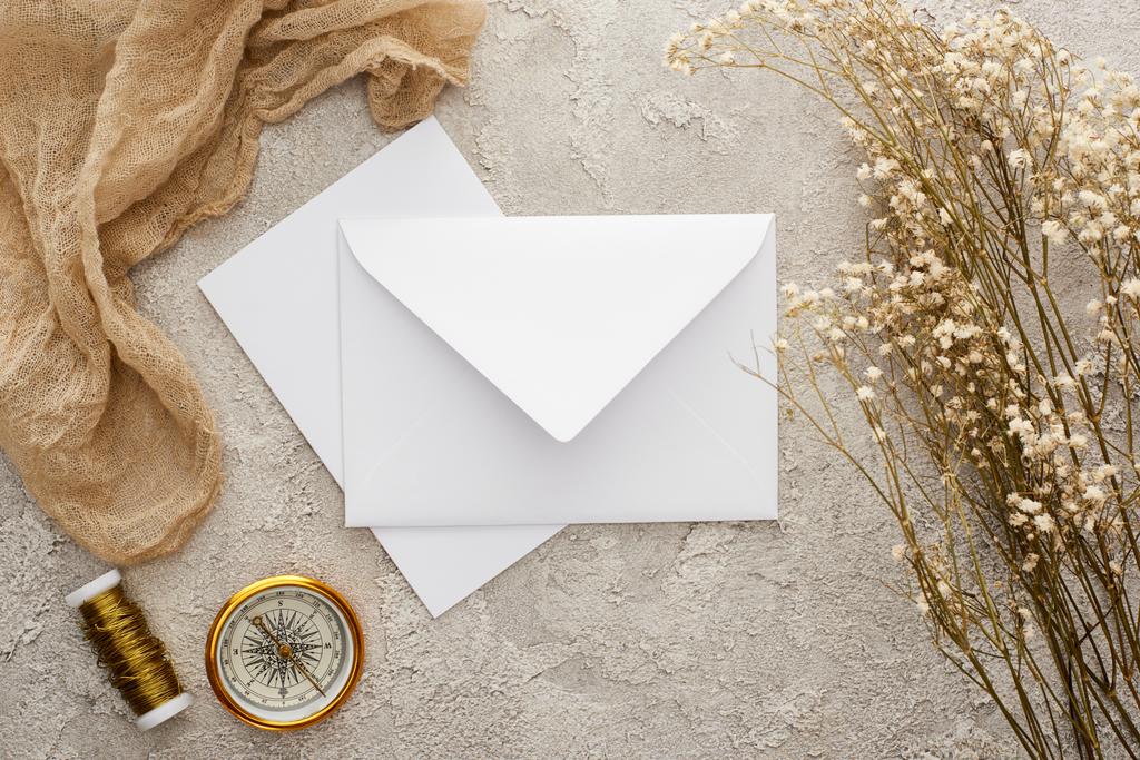 верхний вид на белый конверт и карту рядом с цветами, бежевая мешковина и золотой компас на текстурированной поверхности
 - Фото, изображение