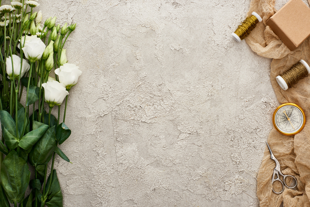 vista dall'alto di fiori di eustoma vicino confezione regalo, bussola, forbici e bobine su sacco beige su superficie strutturata
  - Foto, immagini