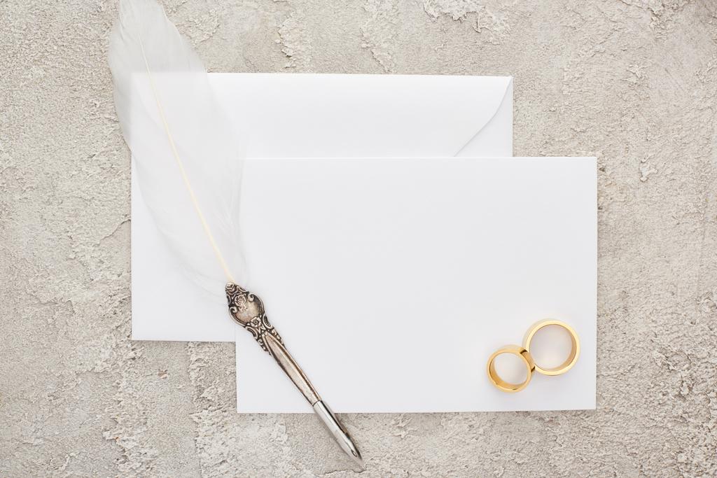 vue de dessus des anneaux de mariage et stylo plume sur carte blanche vide sur surface texturée
  - Photo, image