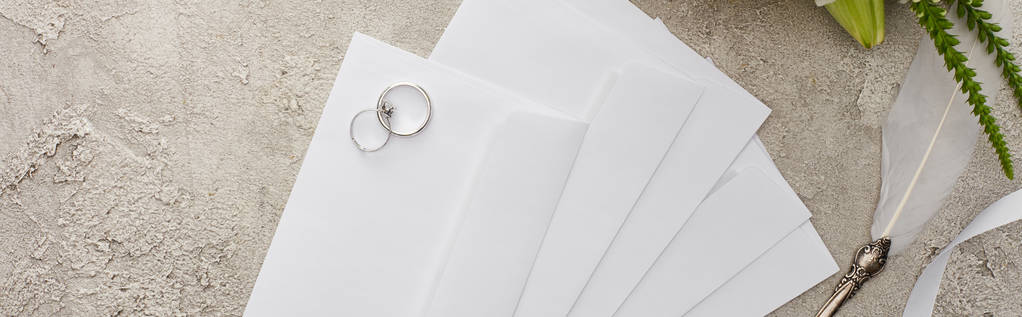 panoramic shot of wedding rings on envelopes near quill pen on textured surface  - Photo, Image