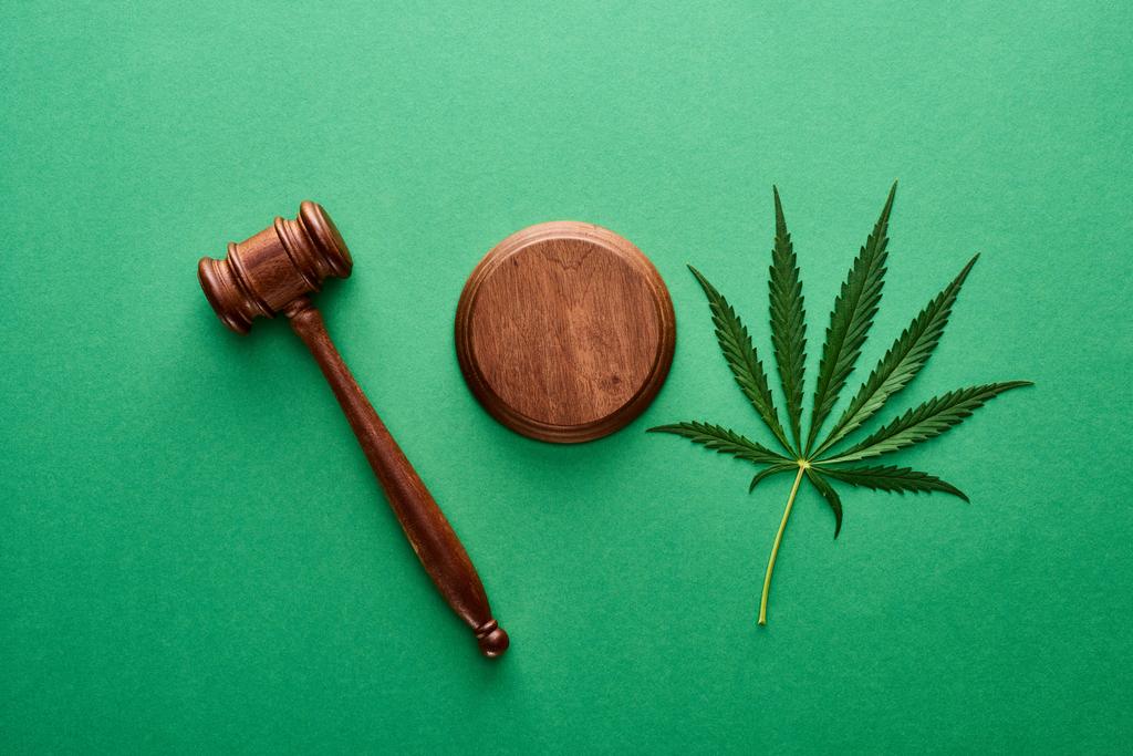 top view of green marijuana leaf with wooden gavel on green background - Photo, Image