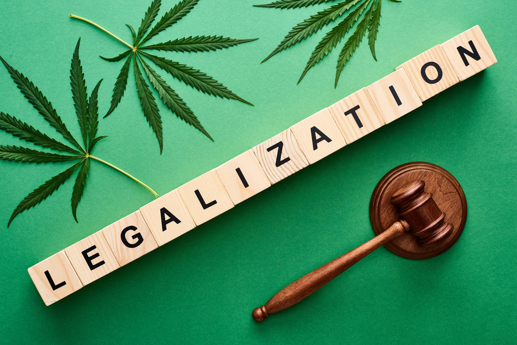 vista superior de folhas de cannabis verde e palavra de legalização em blocos de madeira perto do martelo no fundo verde
 - Foto, Imagem