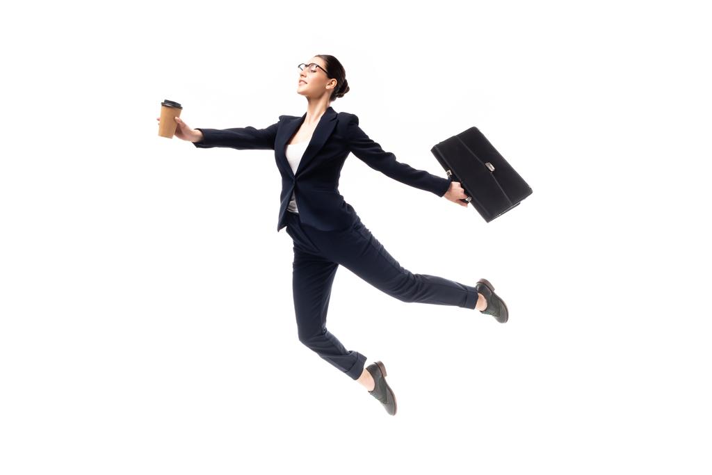 joven atractiva empresaria sosteniendo café para ir y maletín mientras levita aislado en blanco
 - Foto, Imagen