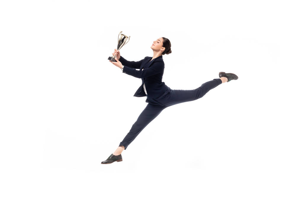 feliz empresaria sosteniendo trofeo taza mientras salta en la danza aislado en blanco
 - Foto, Imagen