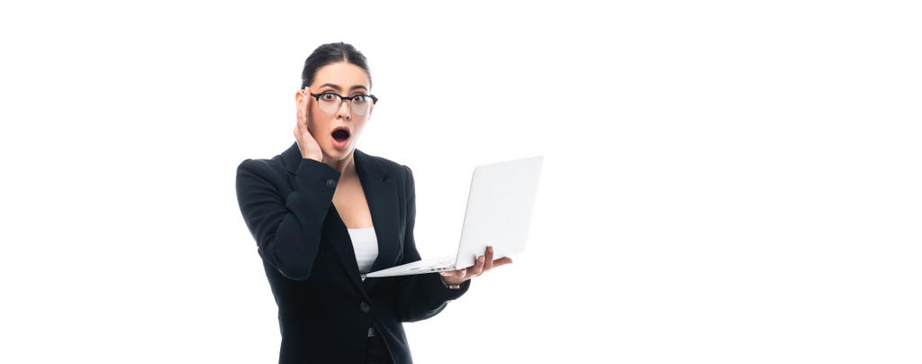 Panoramaaufnahme einer schockierten Geschäftsfrau mit Laptop, während sie isoliert auf weiße Kamera blickt - Foto, Bild