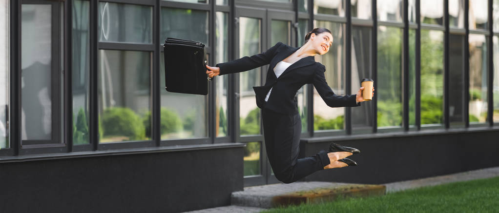 Panoramaaufnahme einer glücklichen Geschäftsfrau, die schwebt, während sie Pappbecher und Aktentasche hält - Foto, Bild
