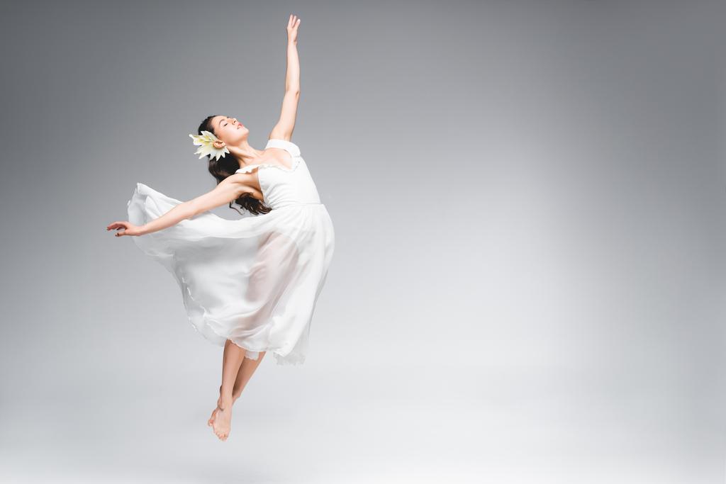 грациозная балерина в белом платье прыгает во время танцев на сером фоне
 - Фото, изображение