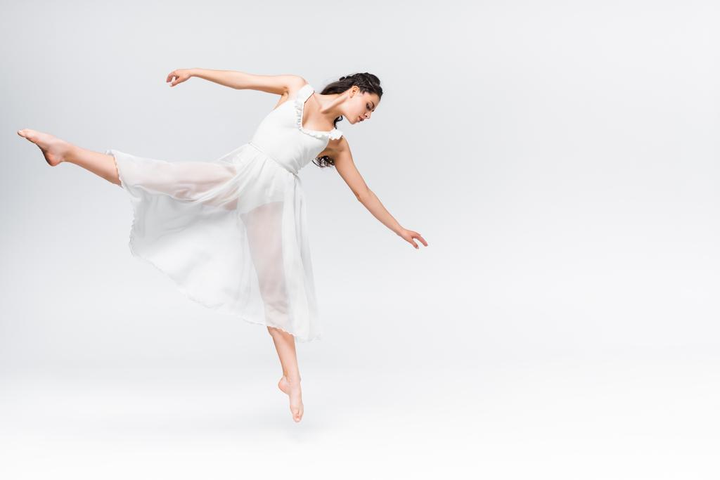 приваблива молода балерина танцює в білій сукні на сірому фоні
 - Фото, зображення