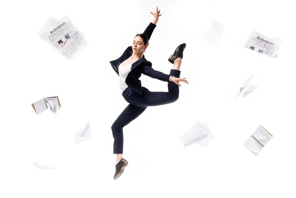 elegante Geschäftsfrau tanzt umgeben von Zeitungen, Notizbüchern und Papieren, die isoliert auf weißem Grund herumfliegen - Foto, Bild
