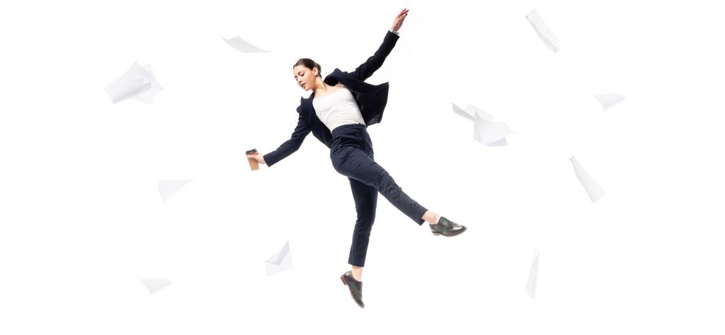 panoramische Aufnahme einer Geschäftsfrau, die Pappbecher in der Hand hält, während sie von fliegenden Papieren umgeben schwebt, isoliert auf weißem Grund - Foto, Bild