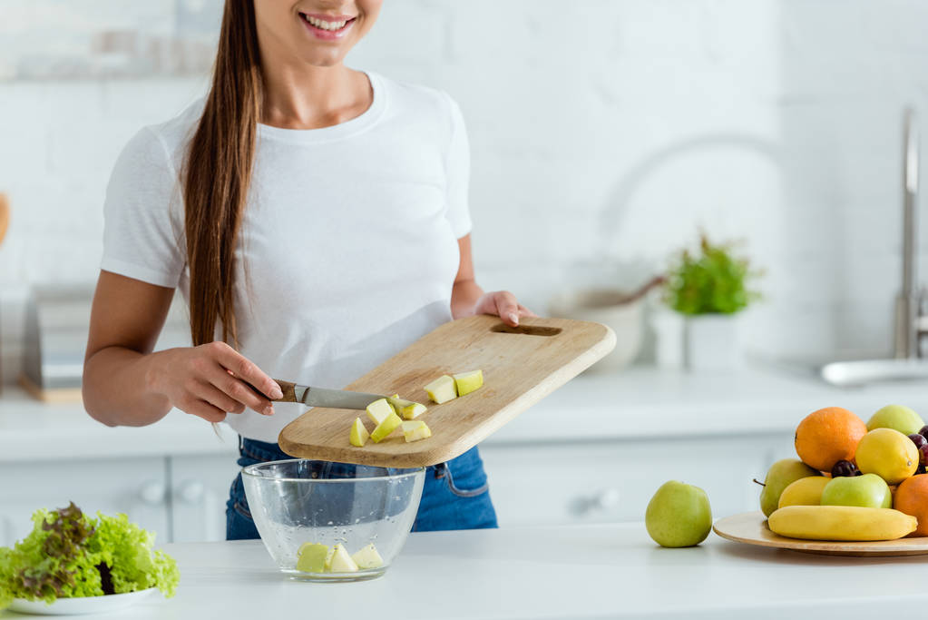 bijgesneden weergave van gelukkige jonge vrouw putting gesneden groene appel in Bowl  - Foto, afbeelding