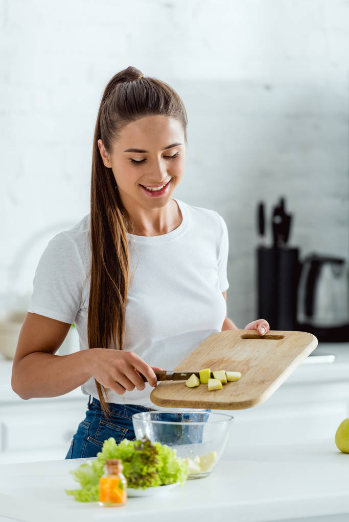 cheerful young woman putting sliced green apple in bowl  - Photo, Image