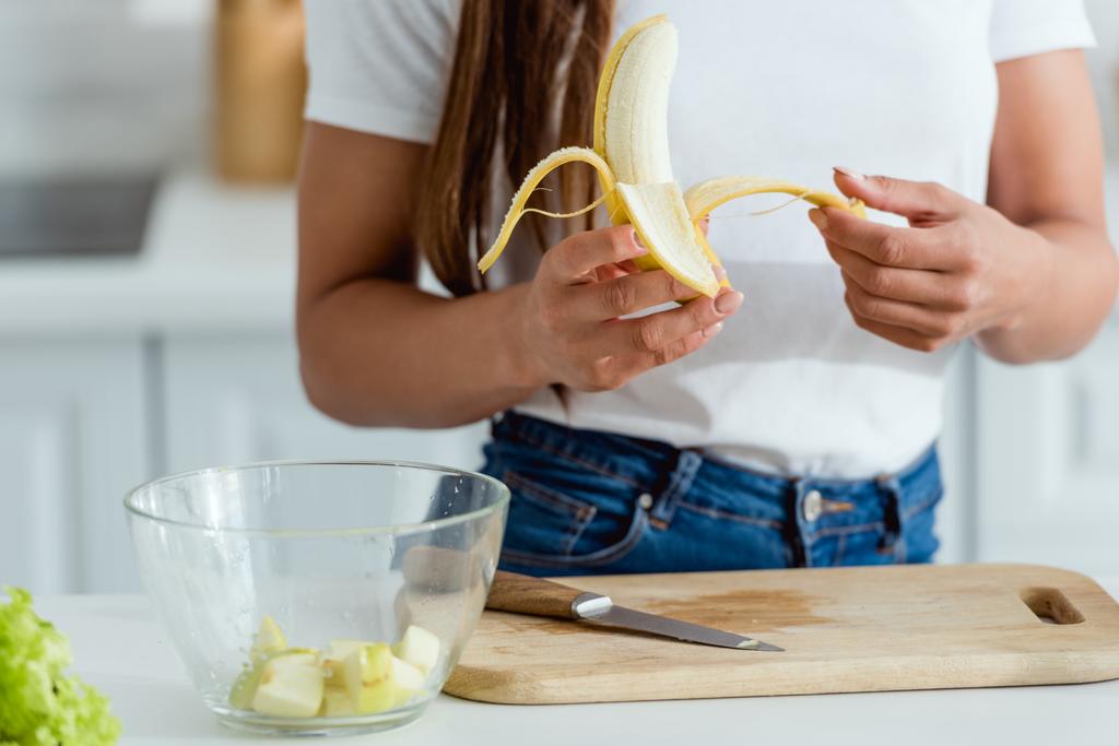 przycięte widok kobiety peeling banana w pobliżu deski do krojenia  - Zdjęcie, obraz
