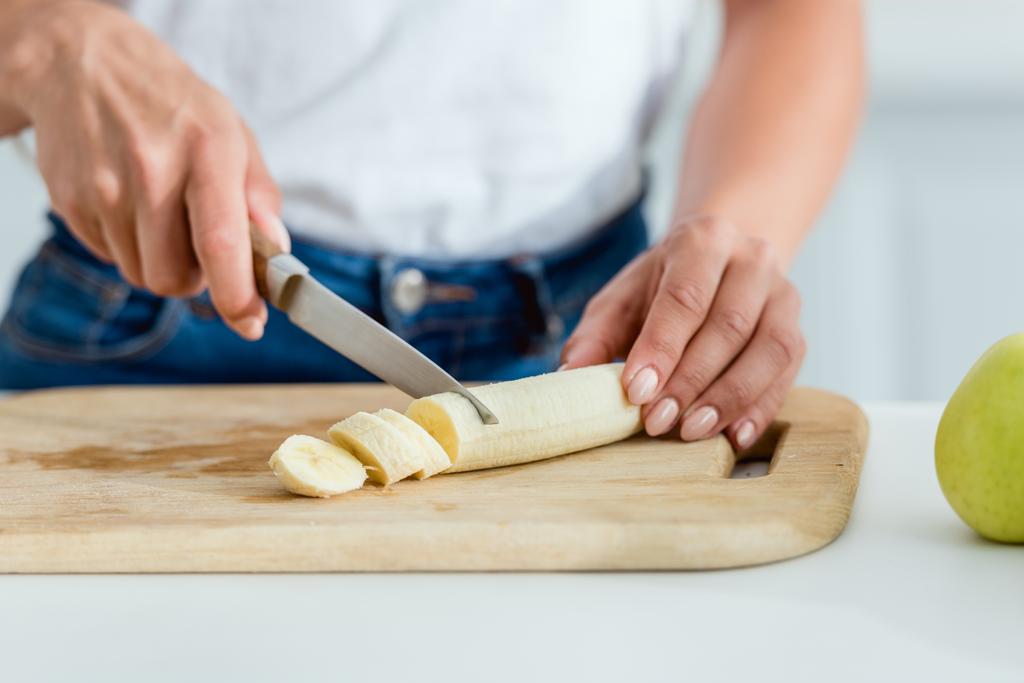 vista ritagliato di donna taglio banana sul tagliere
  - Foto, immagini