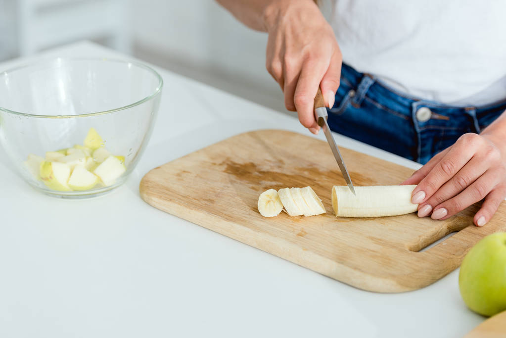 rajattu näkymä nuori nainen leikkaamalla banaani leikkuulauta
  - Valokuva, kuva